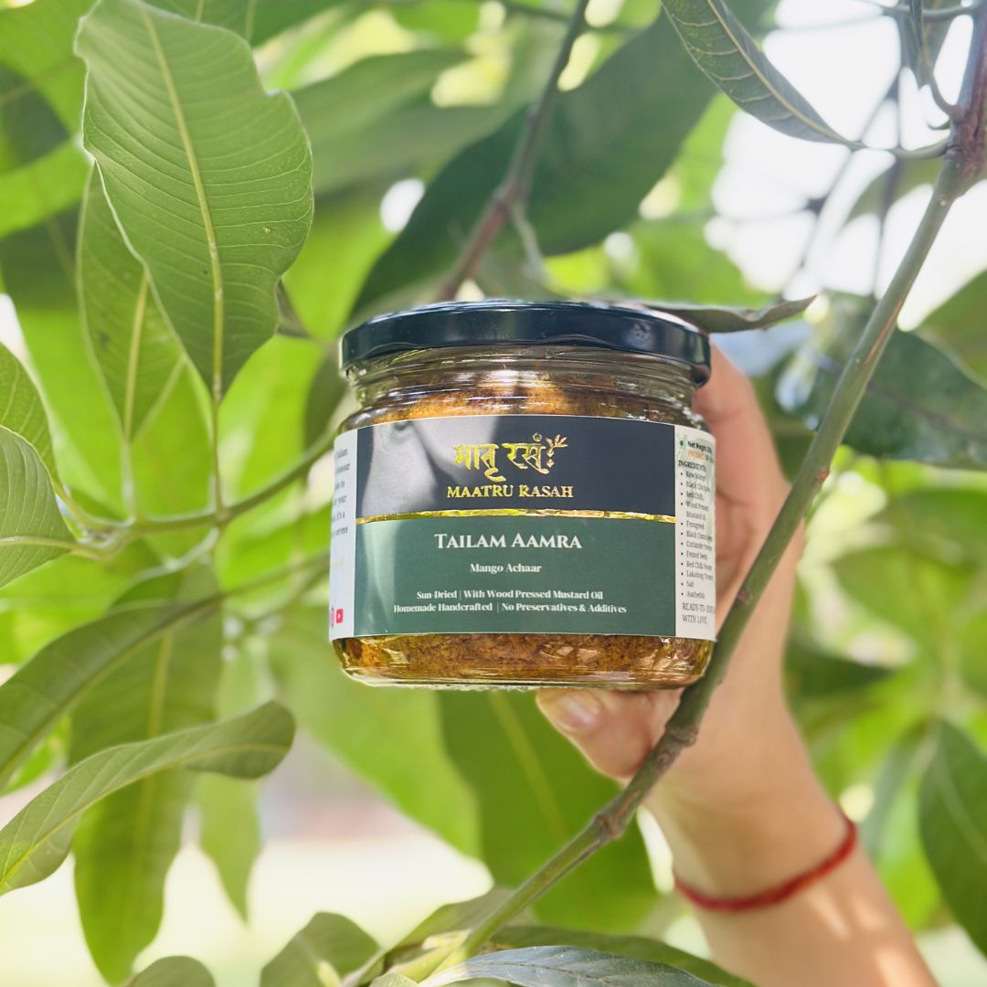 Tailam Aamra mango achaar Tailam Aamra mango pickle in a Maatru Rasah glass jar, held under mango leaves with mustard oil achaar visible.